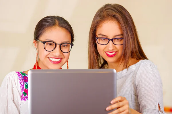 Dwie piękne młode kobiety stwarzające do aparatu, jeden ubrany w tradycyjny Andyjskiej odzieży, drugi w casual ubrania, trzymając laptopa między nimi interakcji patrząc na ekranie, zarówno uśmiechnięty, Park — Zdjęcie stockowe