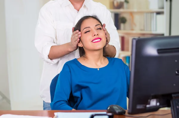 Atrakcyjny brunetka biuro kobieta sobie niebieski sweter siedzi przez biurko odbiera masaż głowy, stress relief koncepcja — Zdjęcie stockowe
