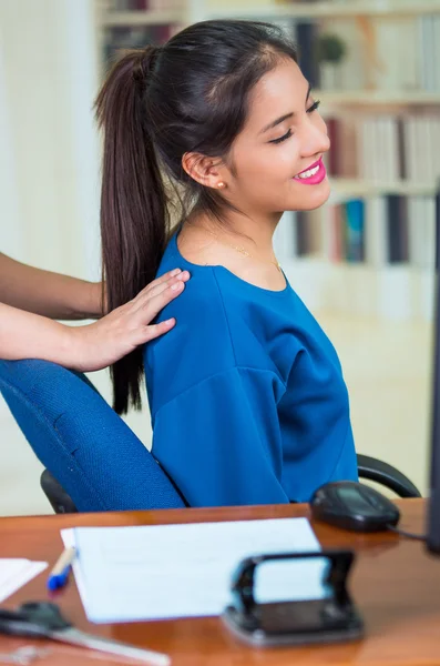 Mulher de escritório morena atraente vestindo camisola azul sentada à mesa recebendo massagem nas costas, conceito de alívio do estresse — Fotografia de Stock
