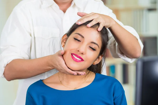 Atrakcyjny brunetka biuro kobieta sobie niebieski sweter siedzi przez biurko odbiera masaż głowy, stress relief koncepcja — Zdjęcie stockowe