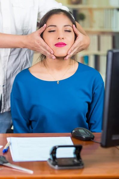 Atractiva morena oficina mujer con suéter azul sentado junto al escritorio recibiendo masaje en la cabeza, concepto de alivio del estrés — Foto de Stock