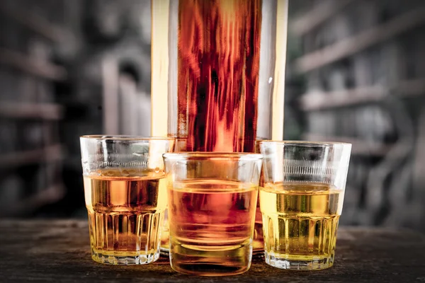 Bottle and glass shots with yellow liqour resembling whiskey, rum, tequila, spirit — Stock Photo, Image