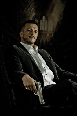 Elegant man sitting in a chair holding  gun over dark background clipart