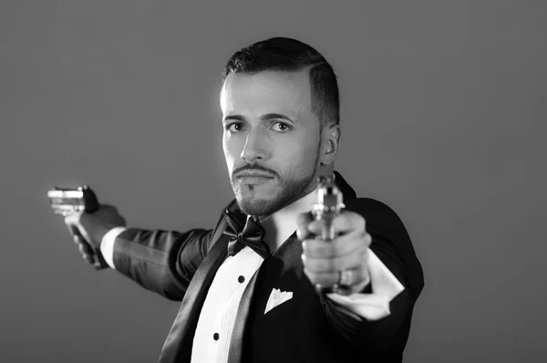 Sexy man in a tuxedo pointing two guns — Stock Photo, Image