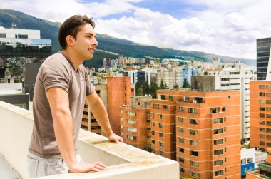 young man looking at Quito city view from balcony clipart