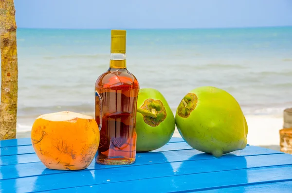 Cocos y botella de licor en la mesa junto a la playa en livingston guatemala — Foto de Stock