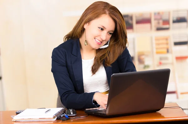 Beautiful young girl working behind a desk with laptop Stock Picture