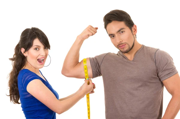 Beautiful girl holding measuing tape around handsome muscular man — Stock Photo, Image