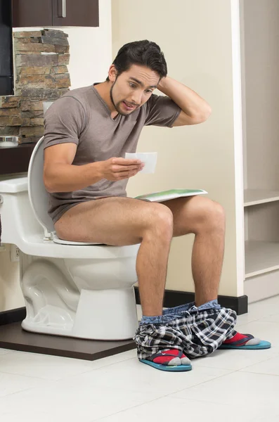 worried man sitting on the toilet running out of paper