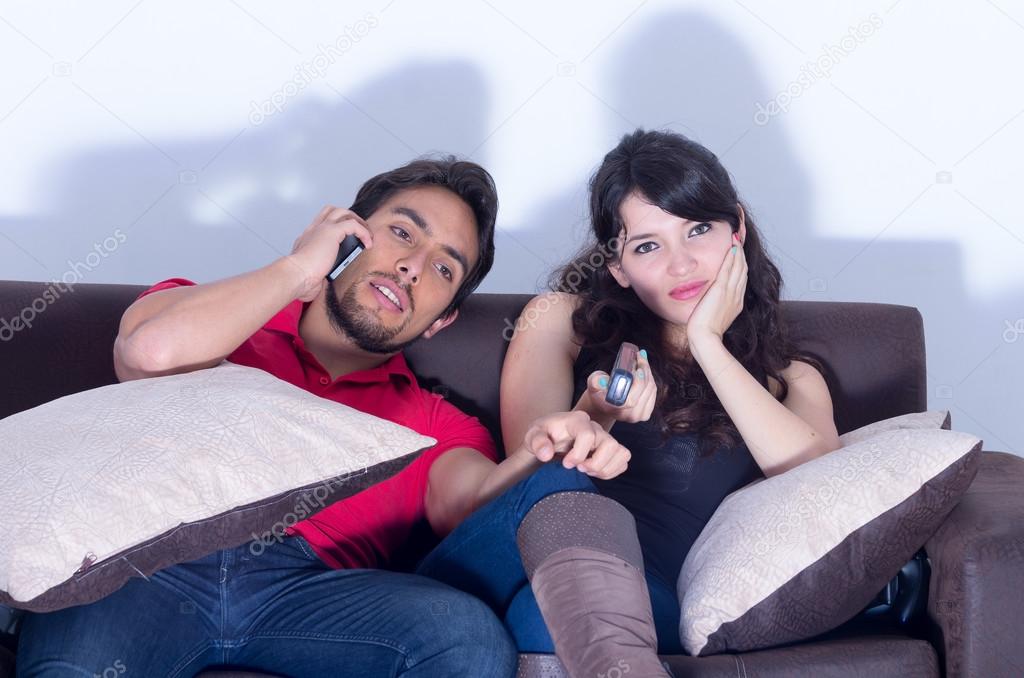 bored girlfriend watching tv while boyfriend chats on the phone