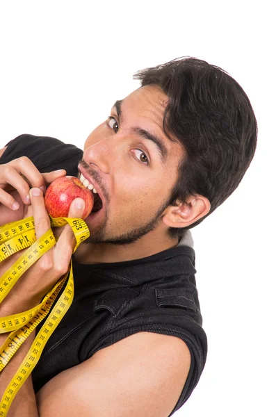 Guapo joven fuerte hombre sosteniendo cinta métrica y mordiendo manzana roja —  Fotos de Stock