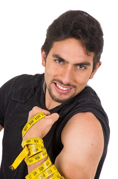 Guapo sonriente joven latino mostrando los músculos envueltos alrededor de cinta métrica — Foto de Stock