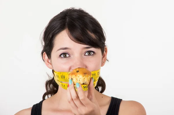 Beautiful young woman with measuring tape around her mouth holding muffin — Stock Photo, Image