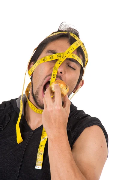 Handsome athletic young man wrapped around measuring tape biting muffin — Stock Photo, Image