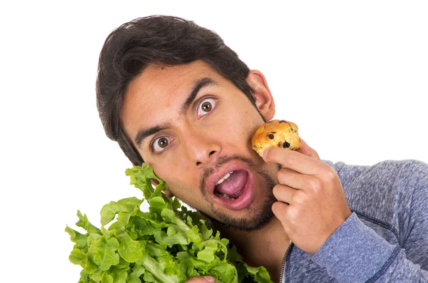 Retrato de primer plano del joven guapo confundido sosteniendo hojas de lechuga fresca y un panecillo —  Fotos de Stock