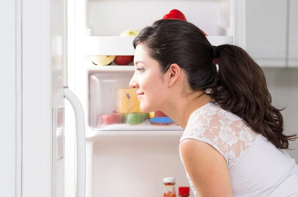 Νεαρή όμορφη γυναίκα που ψάχνει για φαγητό στο ψυγείο — Φωτογραφία Αρχείου