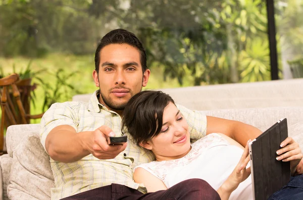 Bonito casal abraço no sofá enquanto assiste tv e usando tablet — Fotografia de Stock