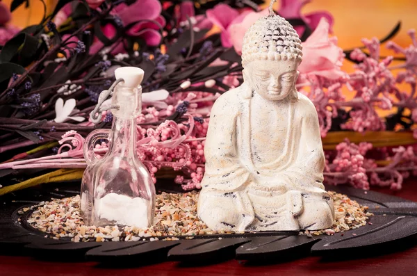 Fles en Boeddha standbeeld met bloemen spa concept — Stockfoto