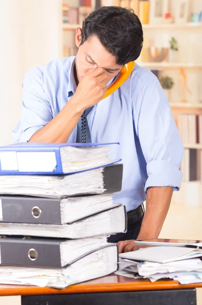 Jeune homme accablé stressé avec des piles de dossiers sur son bureau — Photo