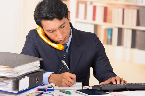 Gestresster junger Mann mit Aktenstapeln auf seinem Schreibtisch überwältigt — Stockfoto