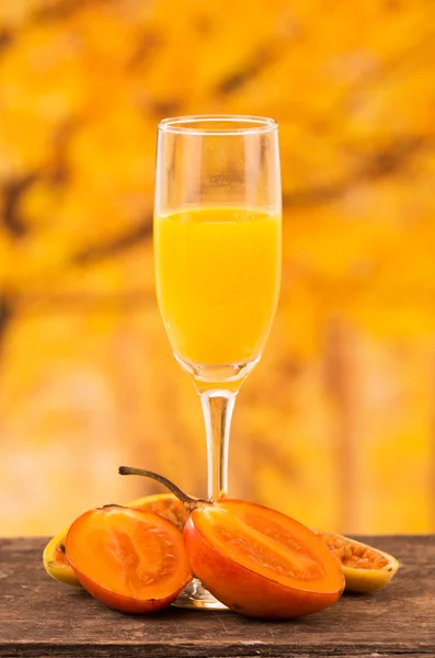 Glass of juice with tree tomato and banana passionfruit slices on a wooden table — Stock Photo, Image