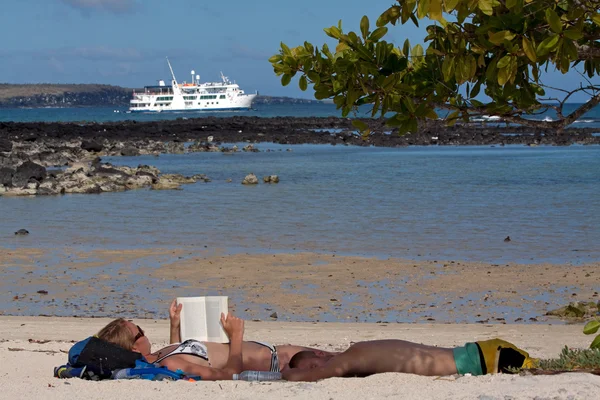 Tourists sunbathing in a beach in the Galapagos Islands, cruise ship in the background — Stock Photo, Image