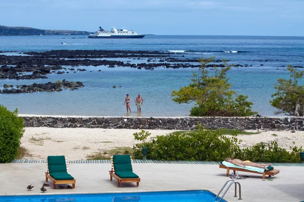 Turister längs stranden njuter av Galapagosöarna, kryssningsfartyg i bakgrunden — Stockfoto