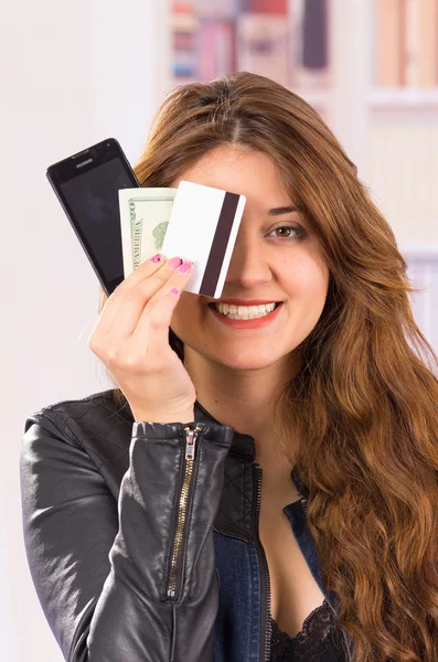 Mujer joven hermosa moderna sosteniendo el teléfono celular, dinero y tarjeta de crédito — Foto de Stock