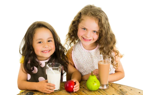 Милые маленькие дошкольницы пьют молоко и едят фрукты. — стоковое фото