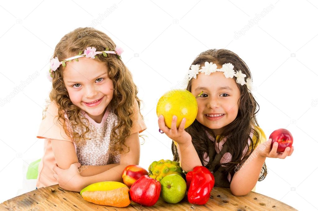 Beautiful healthy little girls holding delicious fresh fruits and vegetables