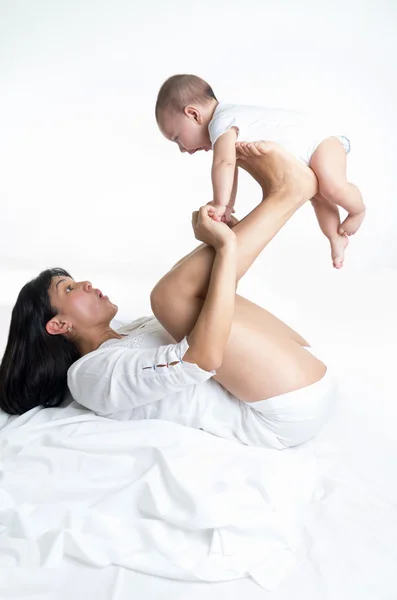 漂亮的妈妈开玩笑地跟她抱着婴儿的手和腿 — 图库照片