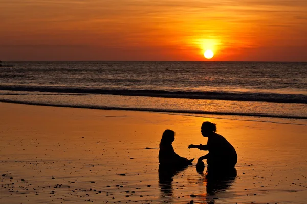 Silhouetten von kleinen Mädchen und Mutter am Strand bei Sonnenuntergang — Stockfoto