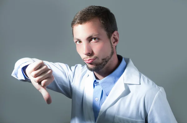 Retrato de primer plano del guapo joven doctor sosteniendo el pulgar hacia abajo — Foto de Stock