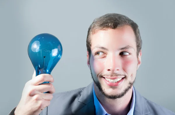 Pohledný mladý inteligentní muž držící Modrou žárovku — Stock fotografie