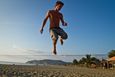 Genç adam Manabi, Ekvator bir plajda slackline Dengeleme silüeti
