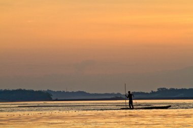 Silhouette of young man in a canoe along the Napo, Yasuni National Park, Ecuador