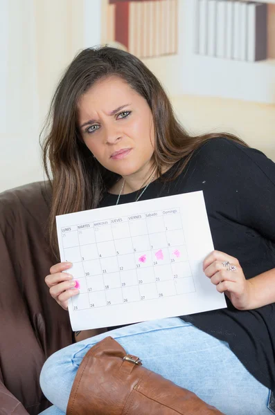 黑发的女孩坐在沙发上举起一个日历 — 图库照片