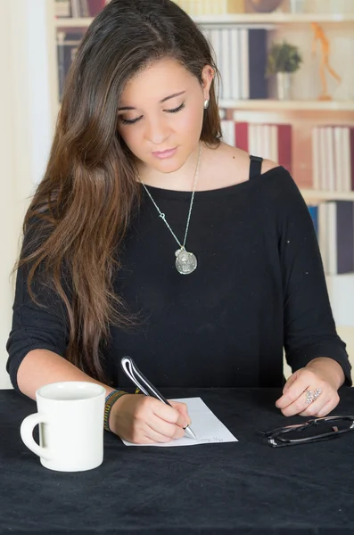 Brunette meisje zitten en schrijven op een papier — Stockfoto