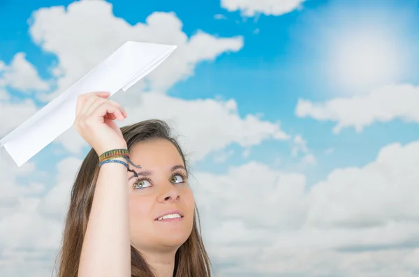 Brunette holding a paperplane in front of cloud themed background — Stock Photo, Image