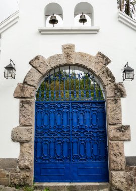Artsy blue painted double gate with grey stones forming an arch on white concrete building