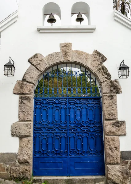 Artsy blue painted double gate with grey stones forming an arch on white concrete building — Stockfoto