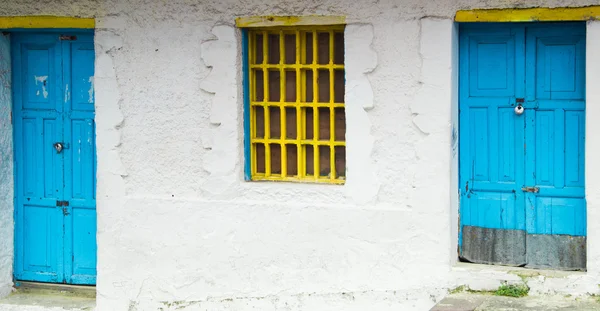 Architettura in stile mediterraneo con barre di metallo giallo che coprono la finestra e le porte azzurre sulla casa bianca — Foto Stock