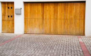 Wooden light colored entrance and garage door with stone tiles in front