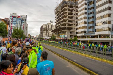 Crowds of people in Quito city street waiting for Pope Francis motorcade to arrive as numerous police officers maintains clear passage and security