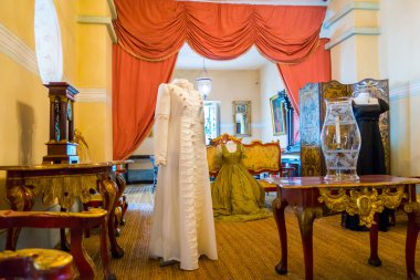Living room decorated  with wooden tables including gold painted details, yellow carpet and a female colonial dress standing up, Bogota Colombia