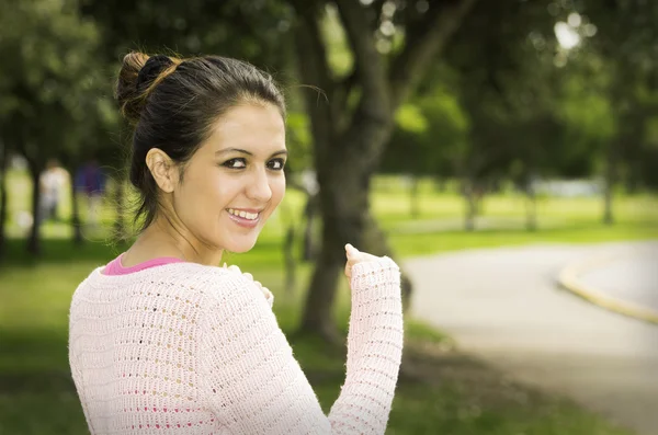 Hispanic brunette model in park wearing white top caption of upper body sideways angle smiling to camera — ストック写真