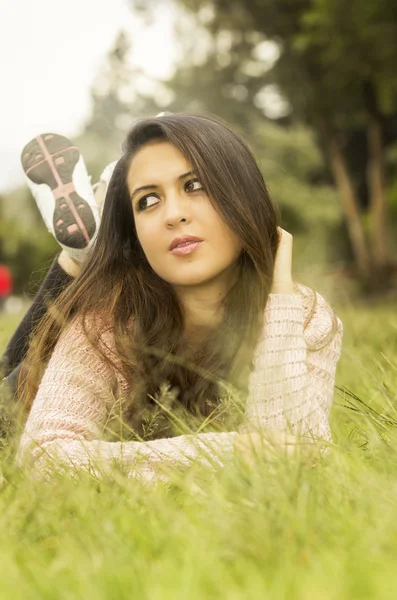 Hispanic model brunette lying on grass facing camera and posing thoughtfully looking to the side — Stok fotoğraf