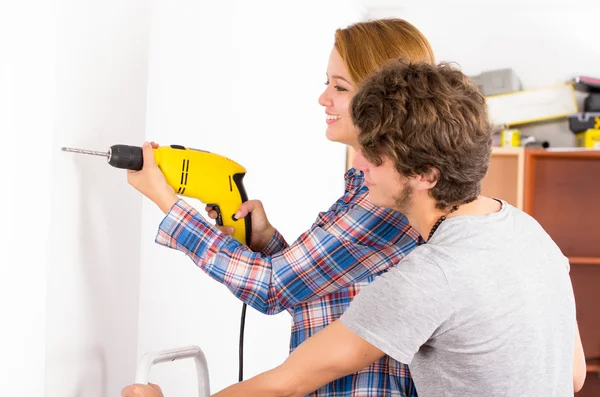 Couple renovating together as woman using power drill on wall with man standing next to her observing — Stok fotoğraf