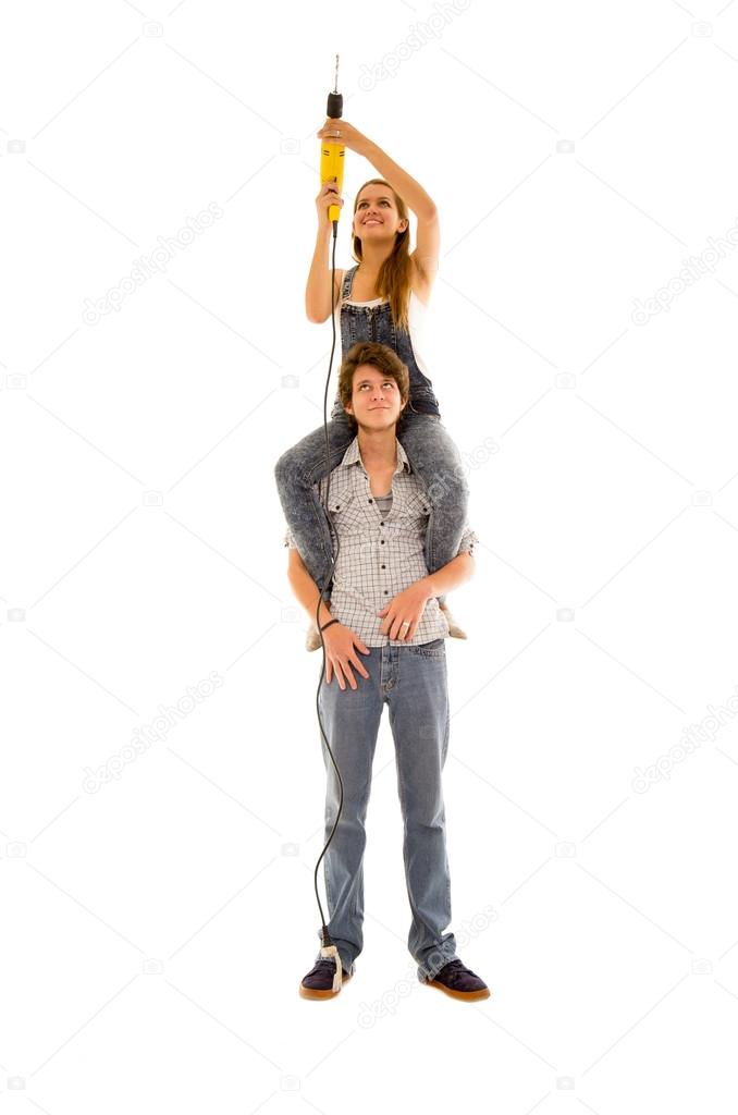 Couple wearing denim working with renovation as woman sitting on mans shoulders and holding up a power drill