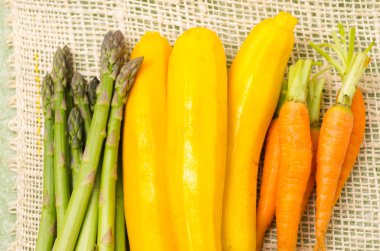 Bunch of brightly colored fresh asparagus, zucchinis and carrots in piles next to each other on a hemp cloth clipart